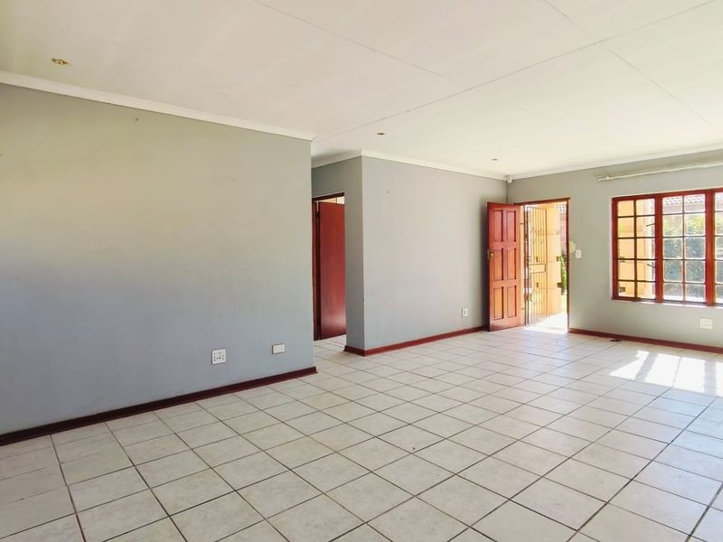 A spacious, empty living area featuring neutral grey walls, tiled flooring, and natural light through a window with security bars.