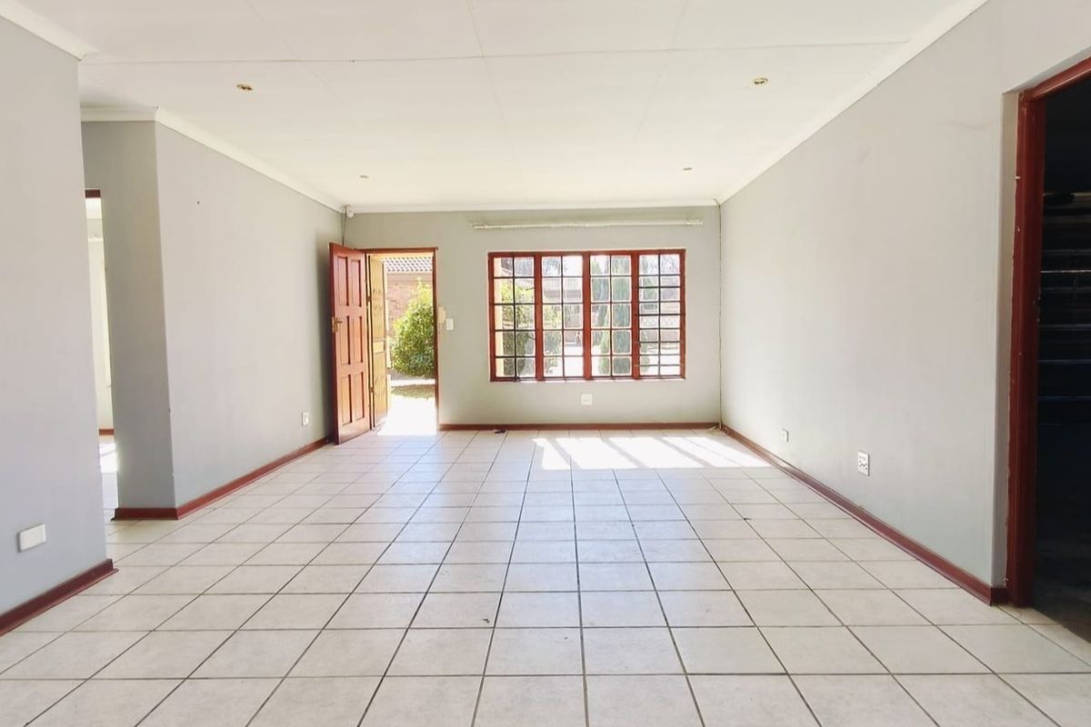 A spacious, empty living area featuring neutral tiled flooring, recessed lighting, and large wooden-framed windows providing natural light and access to the exterior.