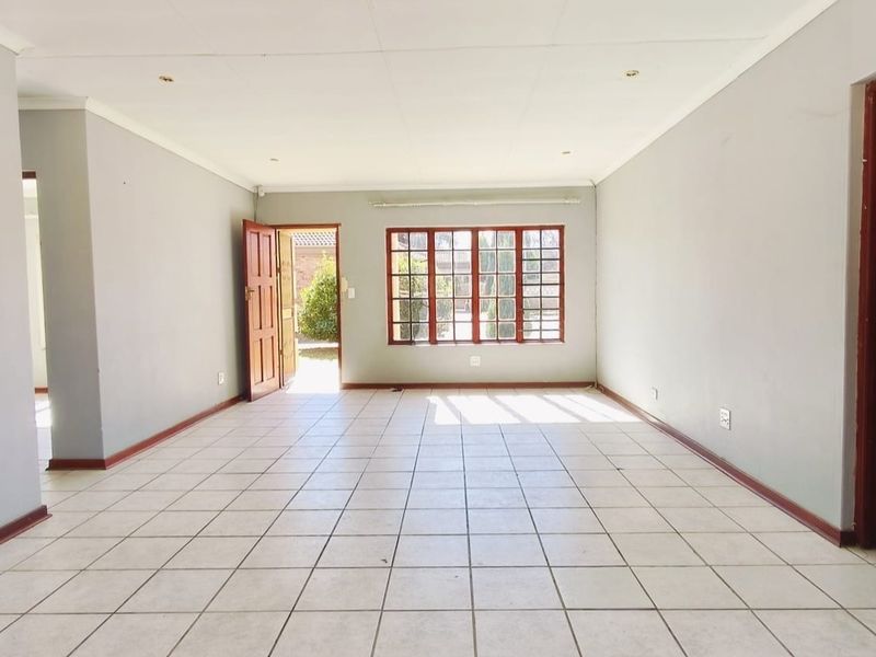 A spacious, empty living area featuring neutral tiled flooring, recessed lighting, and large wooden-framed windows providing natural light and access to the exterior.