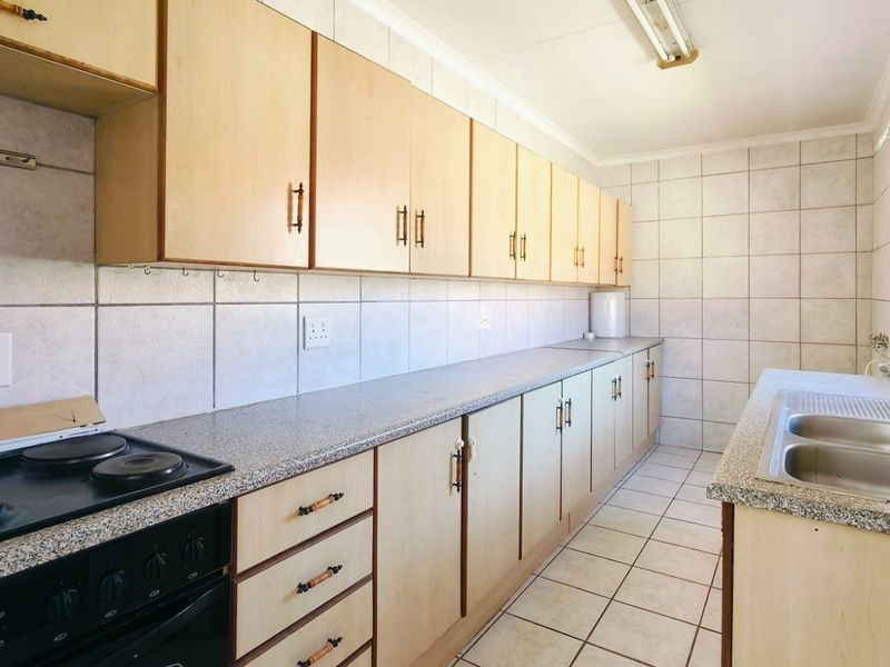 A functional, empty kitchen featuring extensive built-in cabinetry, laminate countertops, a double bowl sink, and an integrated electric stove with tiled splashbacks.