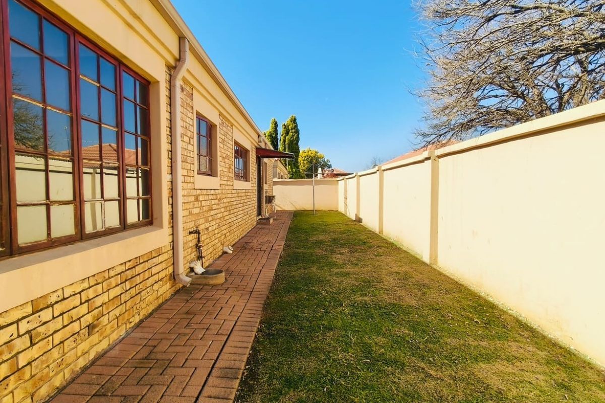 A private rear garden area featuring a paved walkway along the brick townhouse facade and a high perimeter wall for added privacy.