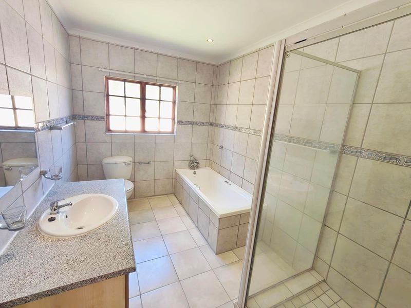 A functional bathroom featuring a built-in vanity, bathtub, separate shower enclosure, and neutral wall and floor tiling.