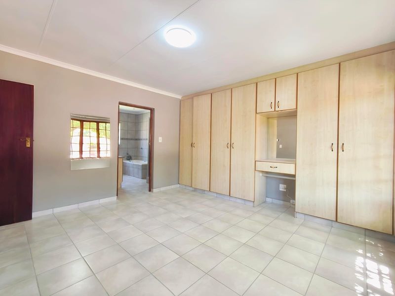 Spacious bedroom featuring neutral tiled flooring, extensive built-in cabinetry with an integrated vanity, and direct access to an en-suite bathroom.