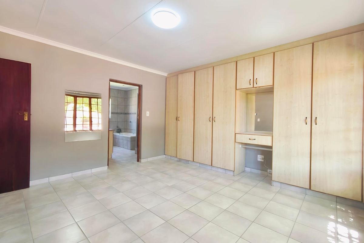 Spacious bedroom featuring neutral tiled flooring, extensive built-in cabinetry with an integrated vanity, and direct access to an en-suite bathroom.