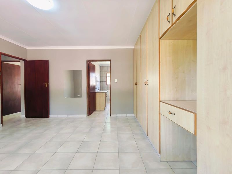 Spacious bedroom featuring neutral tiled flooring, extensive built-in cupboards with an integrated vanity, and direct access to an adjoining room.
