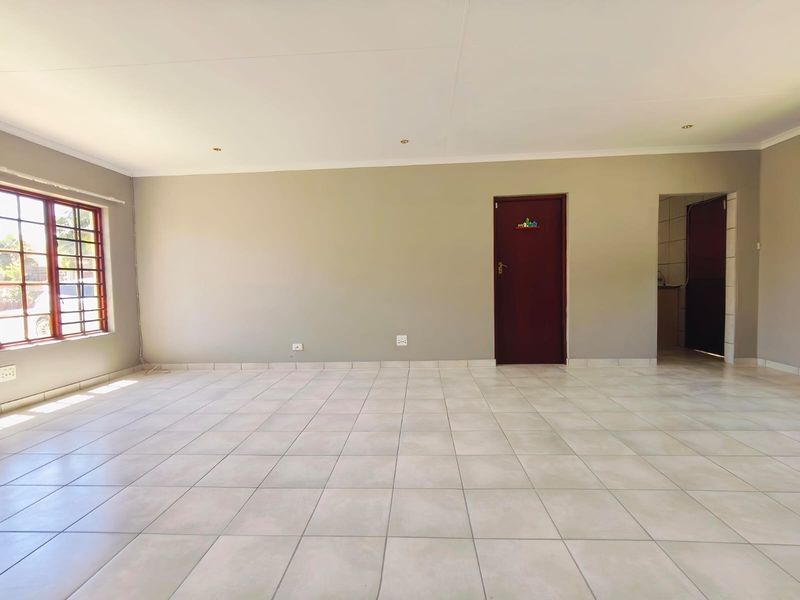 A spacious, empty living area featuring neutral wall tones, tiled flooring, and recessed lighting, offering a versatile blank canvas for interior design.