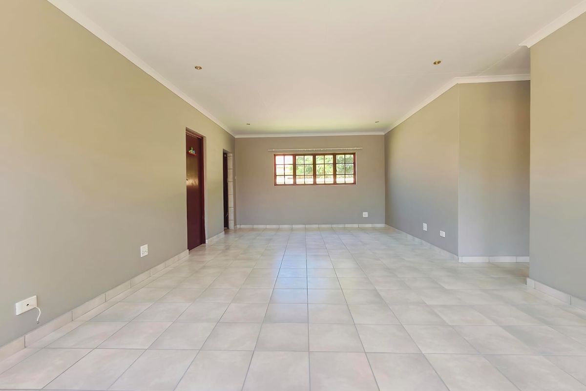 A spacious, empty living area featuring neutral wall tones, tiled flooring, and a timber-framed window, providing a clean canvas for interior design.