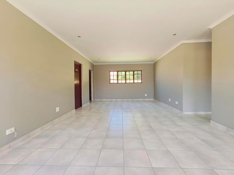 A spacious, empty living area featuring neutral wall tones, tiled flooring, and a timber-framed window, providing a clean canvas for interior design.
