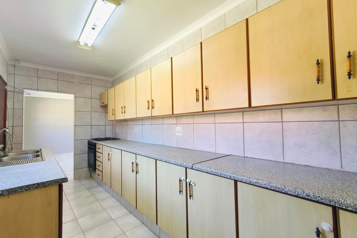 A functional kitchen featuring extensive laminate cabinetry, granite-look laminate countertops, a stainless steel sink, and neutral ceramic wall and floor tiling.