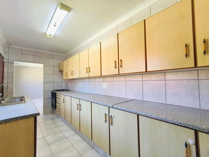 A functional kitchen featuring extensive laminate cabinetry, granite-look laminate countertops, a stainless steel sink, and neutral ceramic wall and floor tiling.
