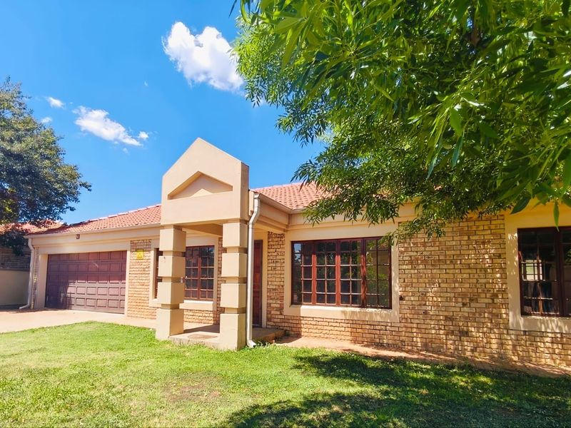 Front elevation of a face brick townhouse featuring a tiled roof, covered entrance, and integrated double garage set within a landscaped garden.
