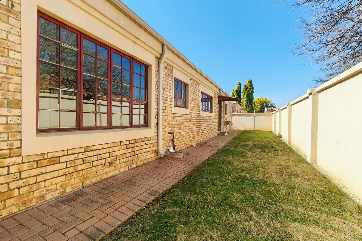 A view of the rear exterior of the townhouse featuring a brick facade, paved walkway, and a private garden area enclosed by a perimeter wall.