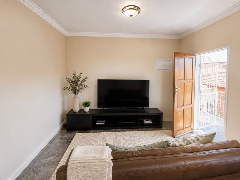 A well-maintained living room featuring tiled flooring, decorative ceiling cornicing, and direct access to an outdoor balcony through a timber door with security gate.