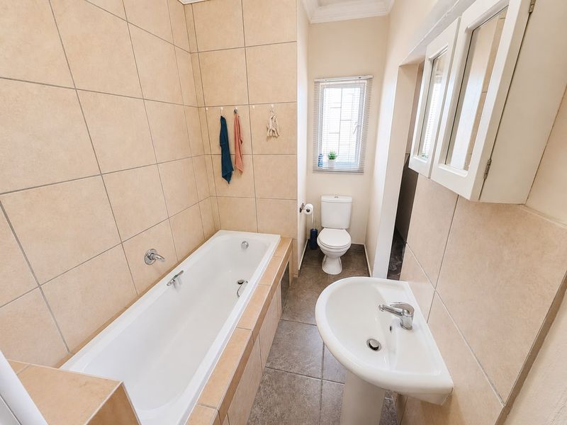 A functional bathroom featuring a tiled bathtub, pedestal basin, toilet, and wall-mounted medicine cabinet with neutral tiling throughout.
