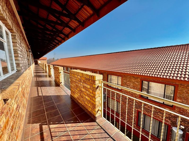 A spacious, covered balcony featuring tiled flooring, brick balustrades, and metal railings, offering an open-air walkway along the apartment building exterior.