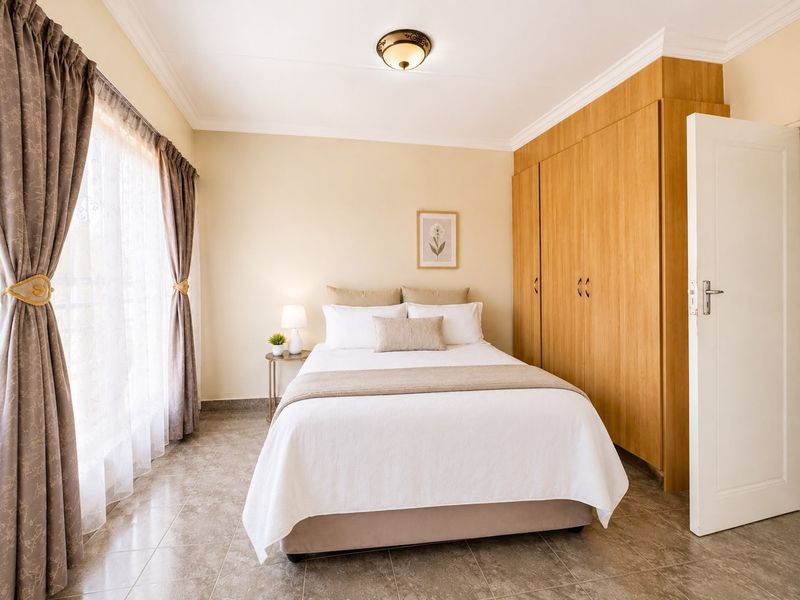 A well-maintained bedroom featuring neutral walls, tiled flooring, and ample built-in cupboard storage with natural light from the large window.