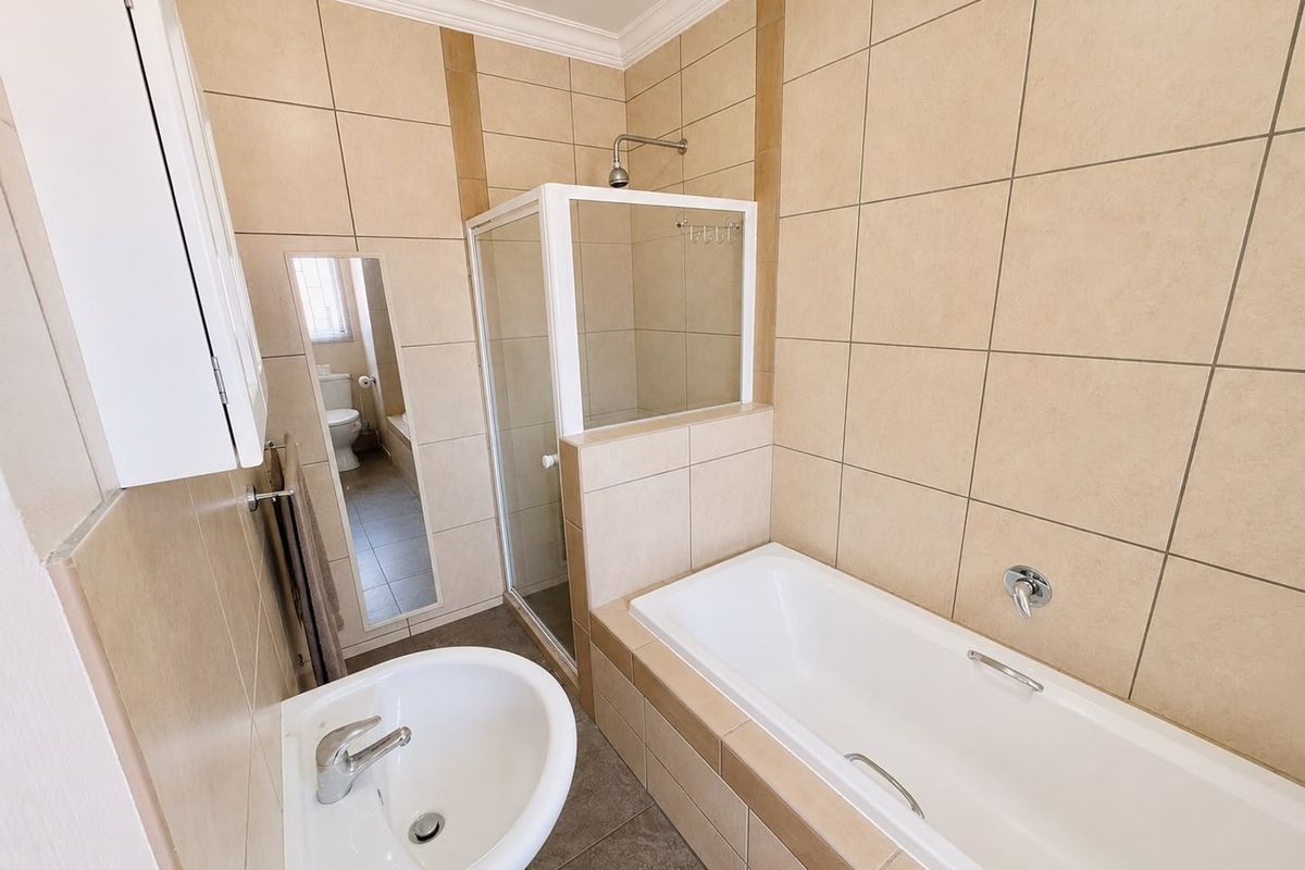 A clean, functional bathroom featuring a separate shower enclosure, a bathtub, and a pedestal basin with neutral wall and floor tiling.
