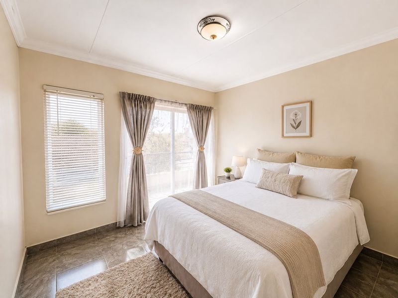 A well-maintained bedroom featuring tiled flooring, a sliding glass door leading to a balcony, and neutral wall tones.