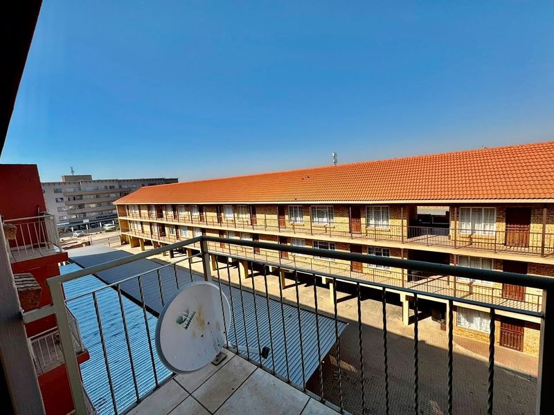 A balcony view overlooking the apartment complex courtyard, featuring tiled flooring and a metal balustrade.