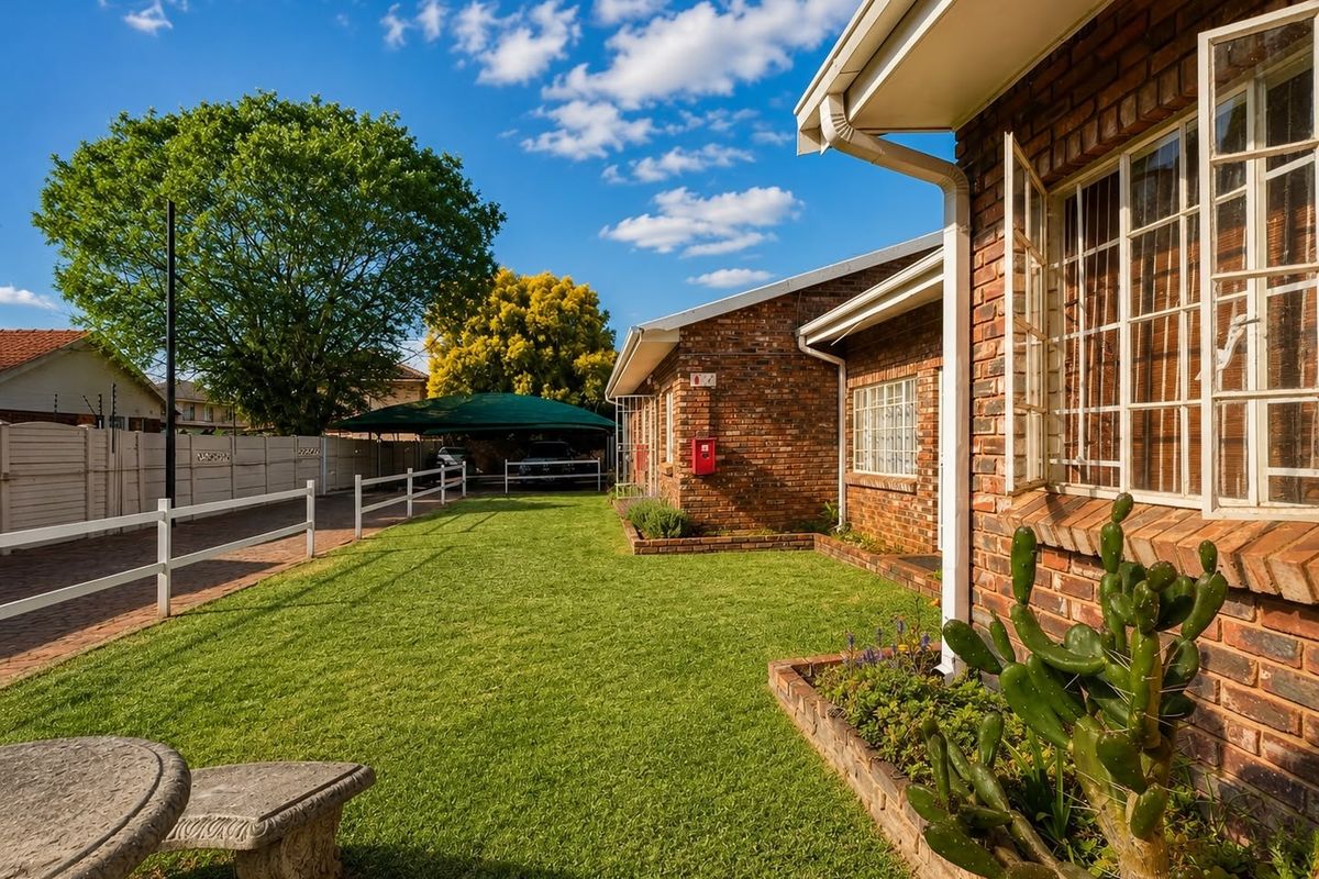 A well-maintained rear exterior view of a face brick apartment building featuring a manicured lawn, paved driveway, and a covered carport area.
