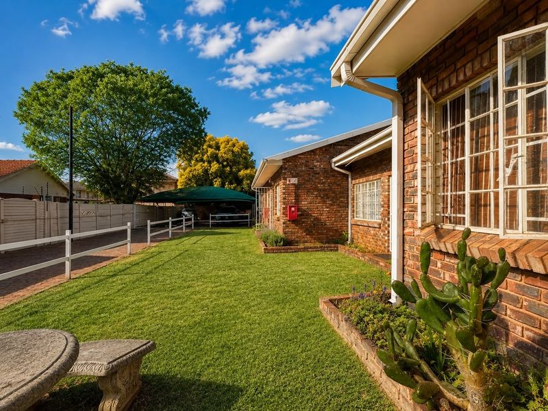 A well-maintained rear exterior view of a face brick apartment building featuring a manicured lawn, paved driveway, and a covered carport area.