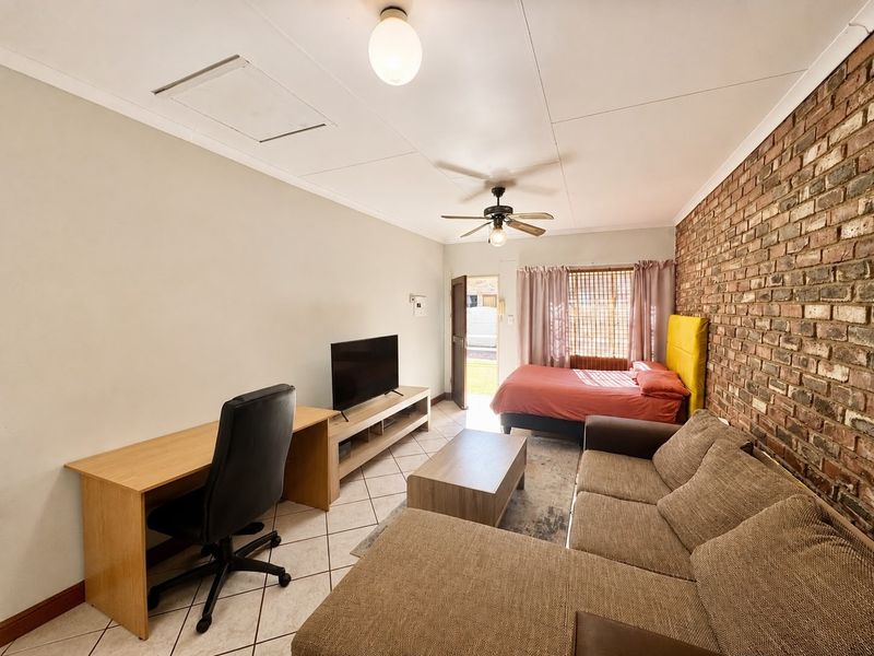 Open-plan living and sleeping area featuring tiled floors, a distinctive exposed brick feature wall, and a ceiling fan.