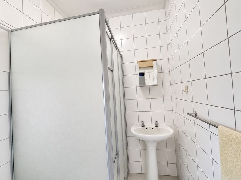 A functional bathroom featuring a shower enclosure, pedestal basin, and white wall tiling.