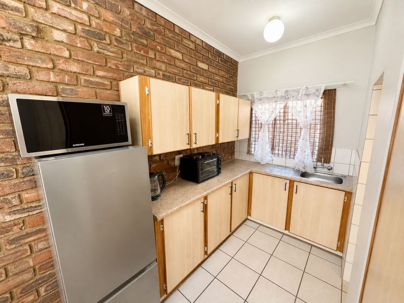 A functional kitchen featuring exposed brick walls, light wood-finish cabinetry, laminate countertops, and ceramic floor tiles.