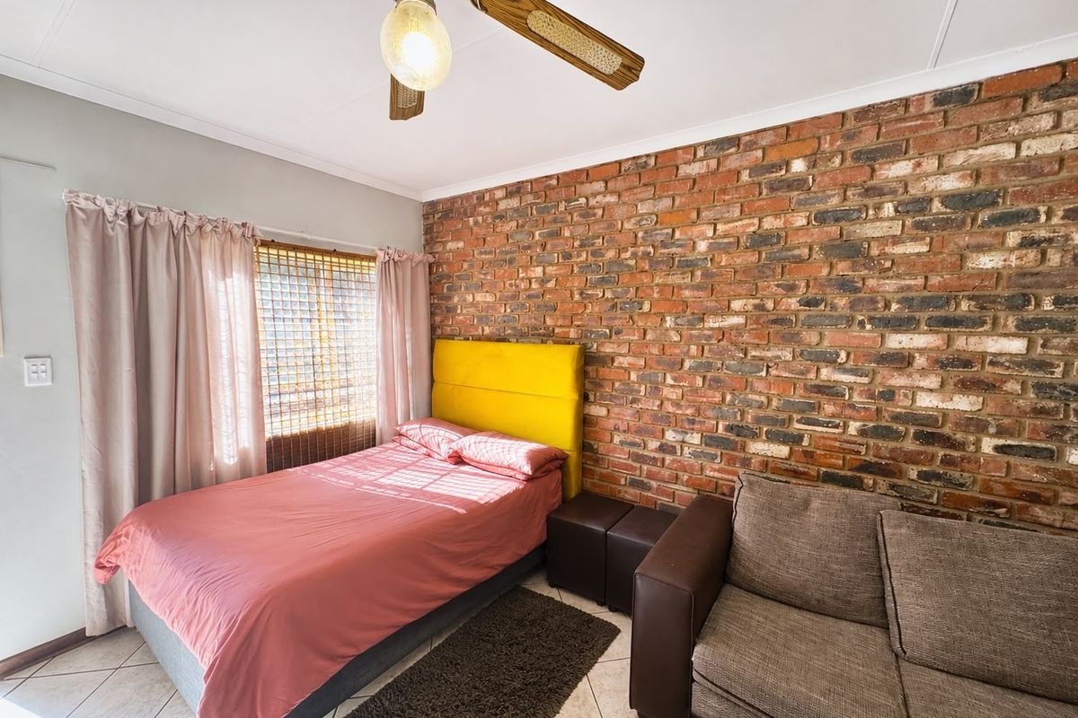 A bedroom featuring an exposed brick feature wall, tiled flooring, and a ceiling fan, offering a rustic aesthetic.