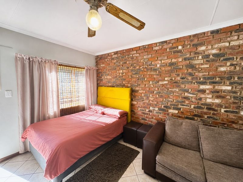 A bedroom featuring an exposed brick feature wall, tiled flooring, and a ceiling fan, offering a rustic aesthetic.