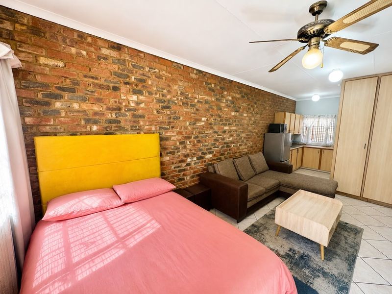 Open-plan studio apartment featuring an exposed brick feature wall, tiled flooring, ceiling fan, and integrated kitchen cabinetry with built-in storage.