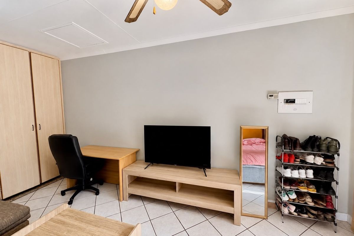 A living room featuring tiled flooring, a ceiling fan, and a built-in wardrobe, providing a functional and neutral space.