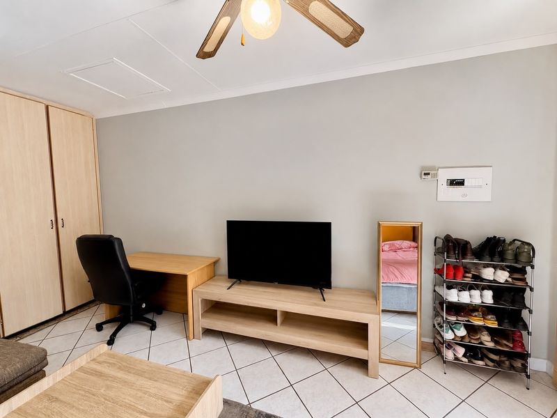 A living room featuring tiled flooring, a ceiling fan, and a built-in wardrobe, providing a functional and neutral space.