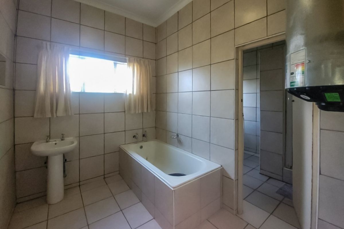 A dated bathroom featuring a pedestal basin, built-in bathtub, and full-height wall tiling, requiring cosmetic updates to modernize the space.
