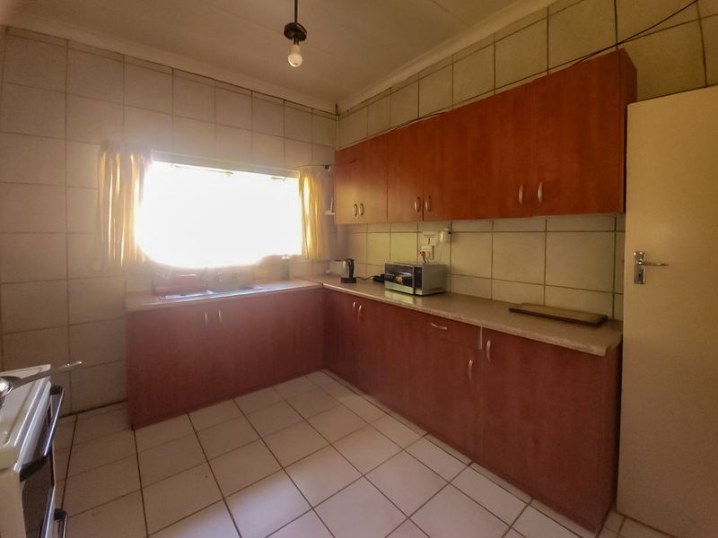 A functional kitchen featuring laminate cabinetry, tiled backsplash, and tiled flooring, offering a dated aesthetic with potential for modern renovation.