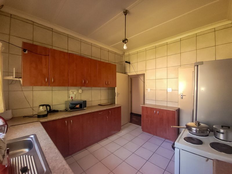 A functional kitchen featuring wood-look cabinetry, tiled splashbacks, and tiled flooring, offering a practical layout with ample storage space.