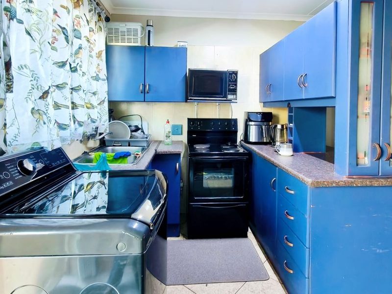 A functional kitchen featuring blue cabinetry, laminate countertops, a tiled backsplash, and a built-in microwave with a freestanding oven.