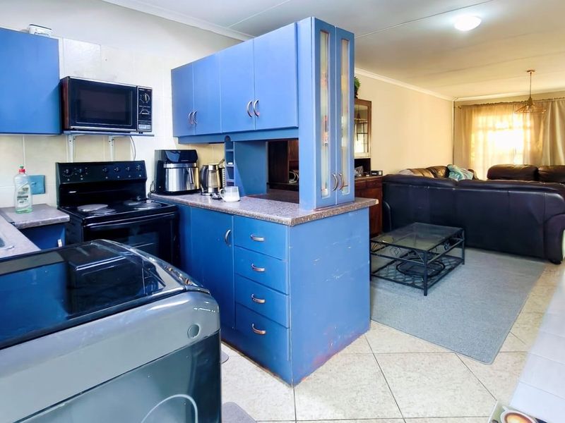 Open-plan kitchen and living area featuring blue cabinetry, laminate countertops, and tiled flooring, offering a functional layout with potential for modern updates.