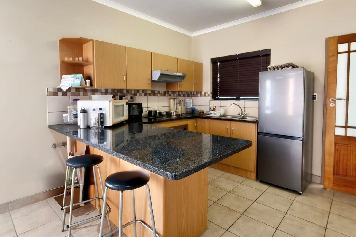 Functional kitchen featuring wooden cabinetry, granite countertops, a breakfast bar, tiled flooring, and a tiled backsplash.