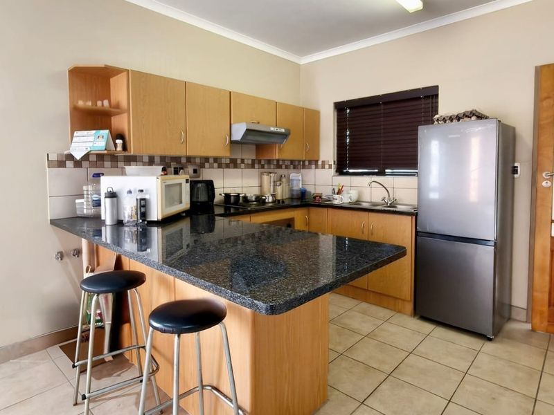 Functional kitchen featuring wooden cabinetry, granite countertops, a breakfast bar, tiled flooring, and a tiled backsplash.