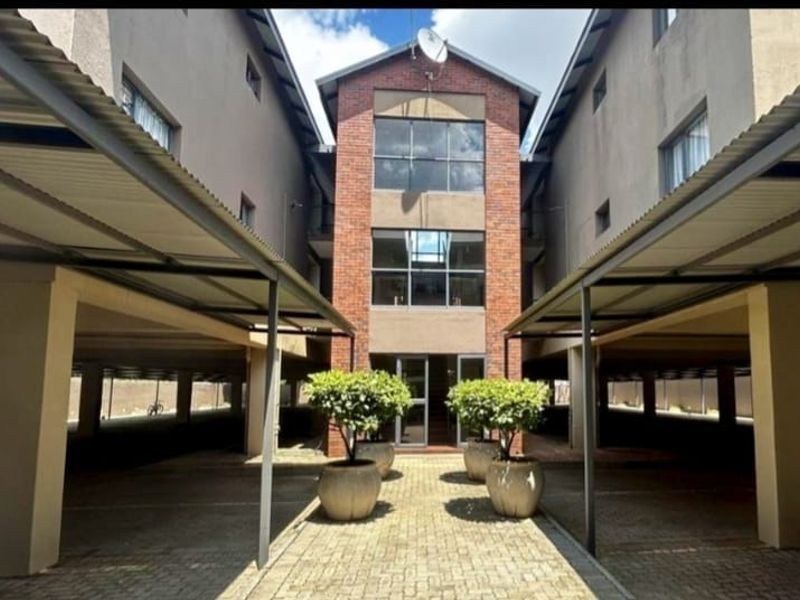 Front view of the apartment complex featuring covered parking bays, a central brick facade entrance, and paved driveway access.