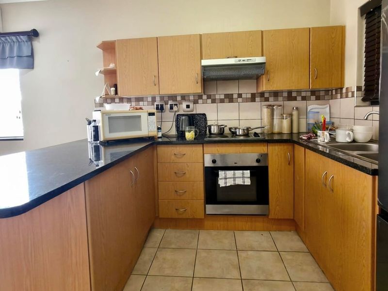 A functional kitchen featuring light wood cabinetry, dark granite countertops, built-in oven, extractor fan, and tiled flooring with a breakfast bar area.