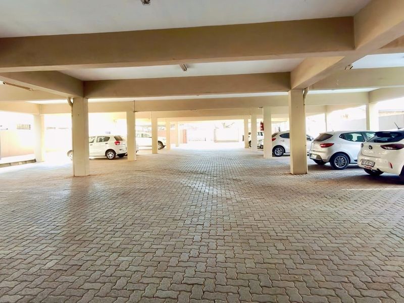 A covered parking garage area featuring concrete structural columns and beams with durable paved flooring.