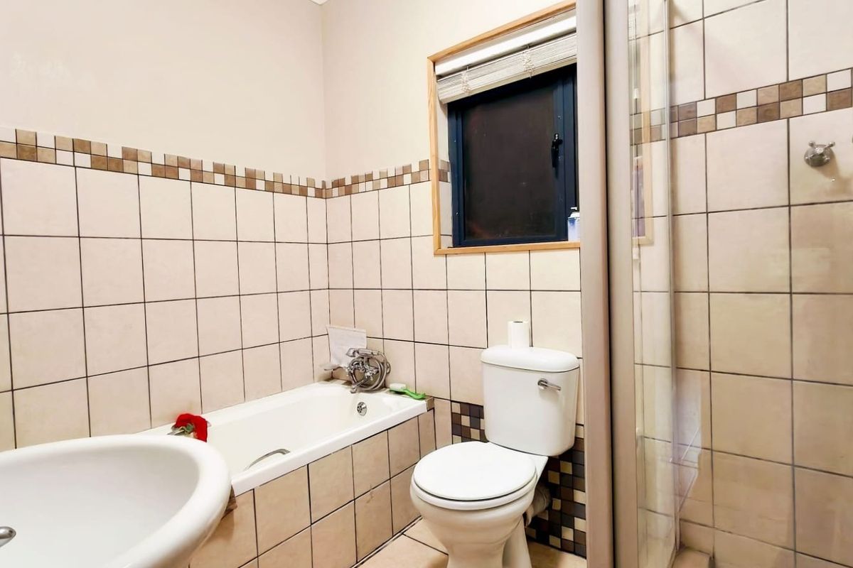 A functional bathroom featuring a bathtub, separate shower enclosure, pedestal basin, and toilet with neutral wall tiling.