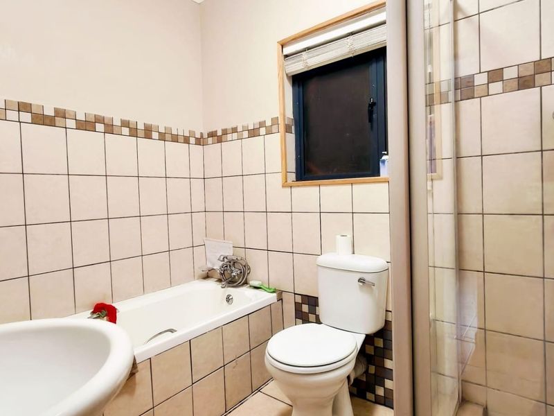 A functional bathroom featuring a bathtub, separate shower enclosure, pedestal basin, and toilet with neutral wall tiling.