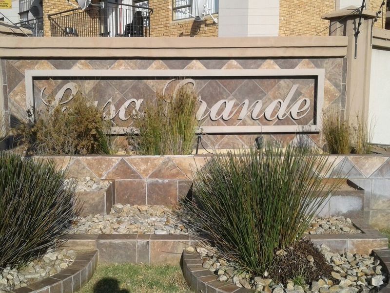 The entrance signage and stone-clad feature wall of the Casa Grande apartment complex, featuring integrated landscaping and perimeter security fencing.