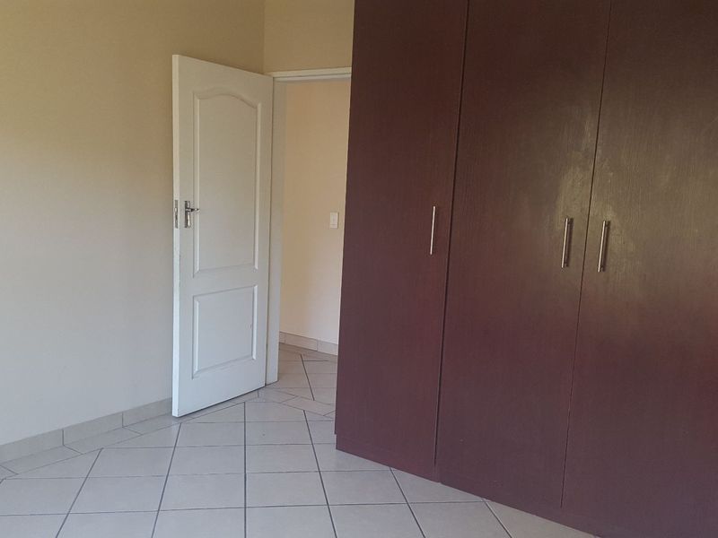 A vacant bedroom featuring neutral walls, tiled flooring, and dark wood-finish built-in cupboards with modern handles.