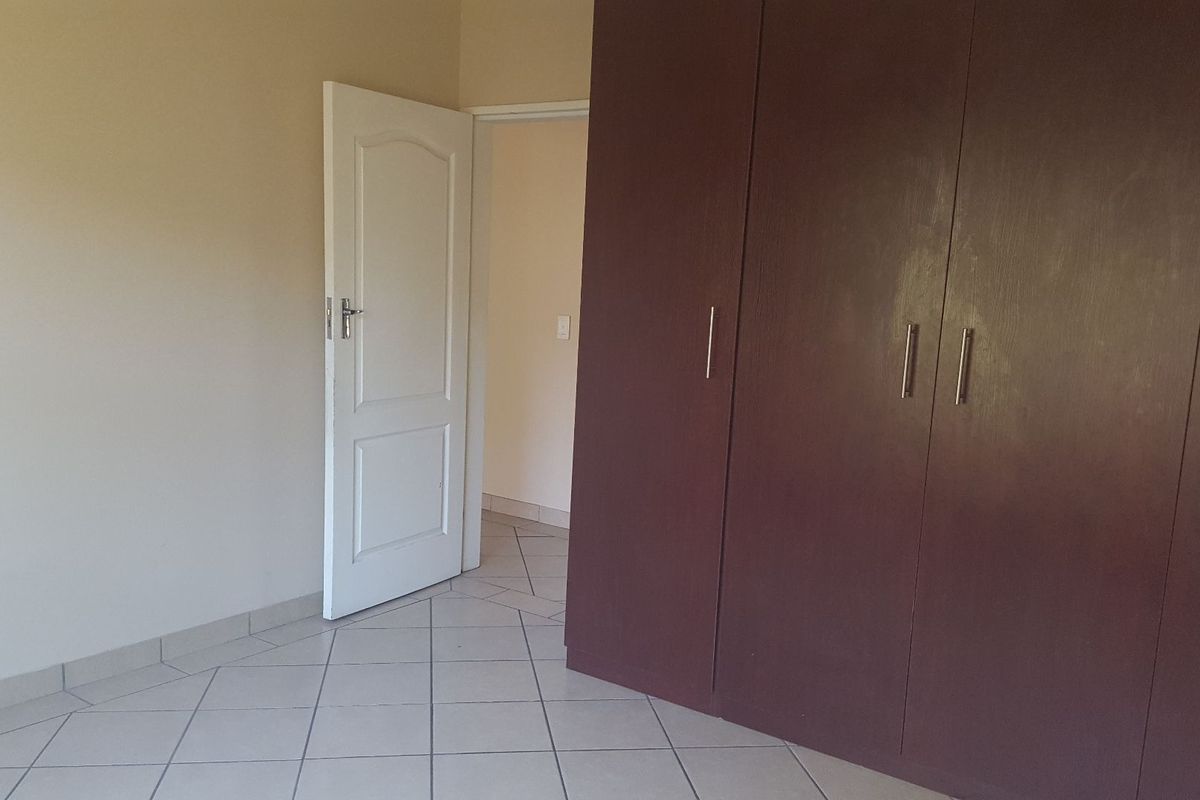 A vacant bedroom featuring neutral walls, tiled flooring, and dark wood-finish built-in cupboards with modern handles.