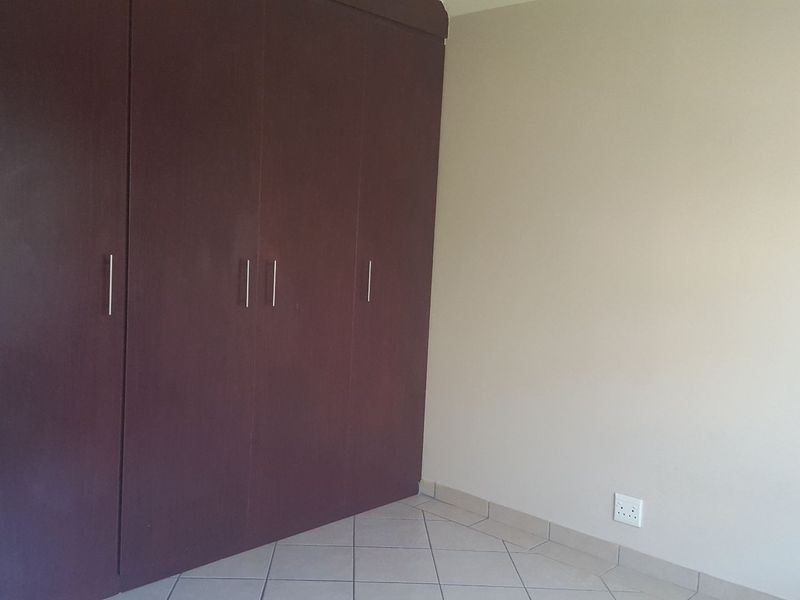 A clean, empty bedroom featuring dark wood-finish built-in cupboards and neutral tiled flooring.