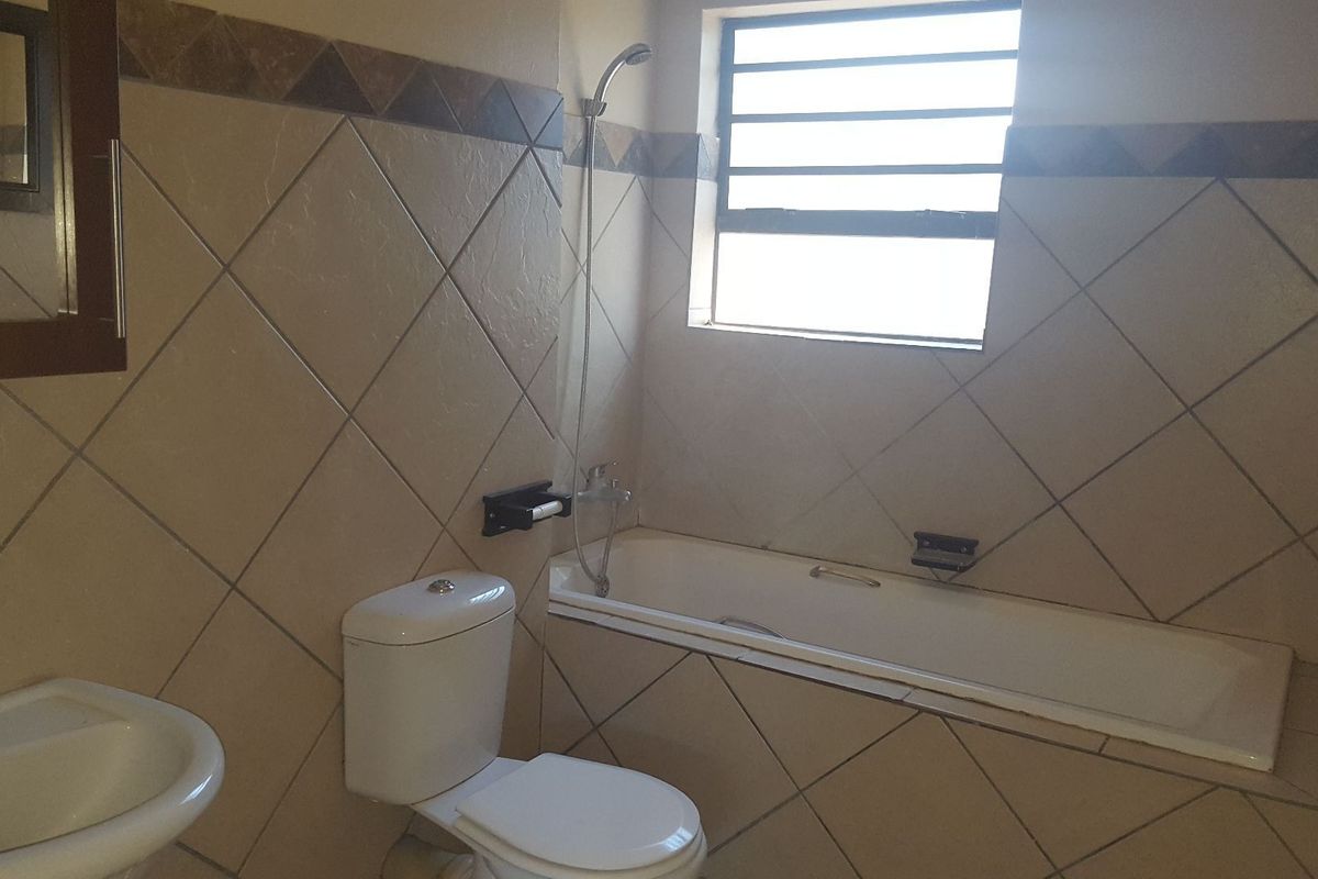 A functional bathroom featuring a bathtub with shower head, pedestal basin, and tiled walls with a louvered window for natural light.